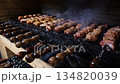Close-up of chicken legs, wings, pork and beef being cooked on a barbecue grill in a restaurant. Juicy meat kebab on skewers. Meat for shish kebab is cooked on fire. The concept of catering. 134820039