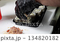 A close-up of a chef wearing gloves, spreading slices of salmon mixed with sauce on sushi before baking, preparing baked sushi in the kitchen of a Japanese restaurant. 134820182