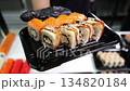 A chef wearing gloves holds up a disposable plate with sliced sushi with eel and salmon in the restaurant's kitchen. The process of making and serving sushi in a restaurant. Sushi delivery. 134820184