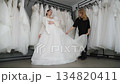 A saleswoman advises a young bride in a wedding shop. The consultant shows the wedding dress to the future bride. Wedding dresses are hung on hangers. 134820411