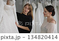 A saleswoman helps a young woman choose a wonderful wedding dress. The bride is in the wedding salon, where there are lots of wedding dresses available in the boutique. 134820414