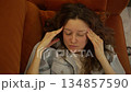 Overhead shot of a young woman dealing with a severe headache, resting on the sofa and gently rubbing her temples. An exhausted individual feeling unwell, enduring the discomfort of a migraine 134857590