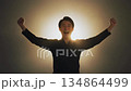 輝く光を背景にガッツポーズで喜びを爆発させる若い男性の笑顔が演出するポジティブでエネルギッシュなイメ 134864499