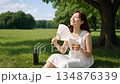 A smiling woman drinking barley tea while fanning herself in a midsummer park | Heat countermeasures, summer daily life image video 134876339