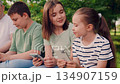 nature surrounds the group while attention stays on phones., digital generation children on mobile screens, they share a moment connected online., screen time for children in the garden, preteens 134907159