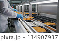 Worker in food processing facility carefully places fried items into trays, showcasing precision and efficiency, camera follows action closely 134907937