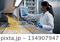 Female technician monitors automated food processing system, observing product flow and adjusting settings, showcasing precision in manufacturing 134907947