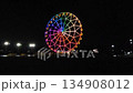 Against the backdrop of a black sky, a beautiful nighttime illumination of a huge Ferris wheel. An evening amusement park. Glowing attractions. 134908012