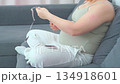 Pregnant woman sitting on a couch using her smartphone in a relaxed home setting. A calm everyday moment highlighting modern maternity lifestyle, comfort, and digital communication during pregnancy 134918601