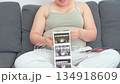 Pregnant woman sitting on a couch using her smartphone in a relaxed home setting. A calm everyday moment highlighting modern maternity lifestyle, comfort, and digital communication during pregnancy 134918609