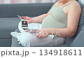 Pregnant woman sitting on a couch using her smartphone in a relaxed home setting. A calm everyday moment highlighting modern maternity lifestyle, comfort, and digital communication during pregnancy 134918611