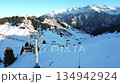 Majestic aerial perspective from a ski lift ascending a snow-covered mountain. Picturesque winter landscape with sunny peaks and pine forests 134942924