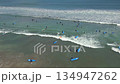 Aerial drone view of surf lessons with beginner surfers paddling and riding small waves near the shore in Bali, Indonesia. Popular surf spot, ocean activity, and tropical beach lifestyle. 134947262