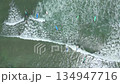 Top-down aerial drone view of beginner surfers paddling, waiting, and catching small waves during surf lessons near the shore. Popular beach activity and tropical surf lifestyle in Bali, Indonesia. 134947716