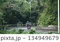 rear view of young asian couple riding bike outdoors on downhill curving rural road 134949679