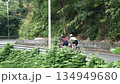 rear view of two young asian women riding bike outdoors on downhill curving rural road 134949680
