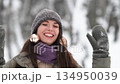 A beautiful young woman in winter clothes is happily spending her free time in a snowy forest. She enjoys the first snow. Active winter recreation. 134950039