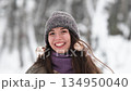 A beautiful young woman in winter clothes is happily spending her free time in a snowy forest. She enjoys the first snow. Active winter recreation. 134950040