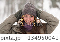 A beautiful young woman in winter clothes is happily spending her free time in a snowy forest. She enjoys the first snow. Active winter recreation. 134950041