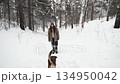A young woman relaxes during a walk in a winter forest with her dog. 134950042