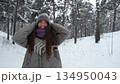 A beautiful young woman in winter clothes is happily spending her free time in a snowy forest. She enjoys the first snow. Active winter recreation. 134950043