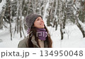 A beautiful young woman in winter clothes is happily spending her free time in a snowy forest. She enjoys the first snow. Active winter recreation. 134950048