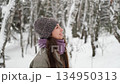 A beautiful young woman in winter clothes is happily spending her free time in a snowy forest. She enjoys the first snow. Active winter recreation. 134950313