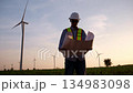 The engineer held the blueprints and looked around the field of wind turbines that were generating electricity. 134983098