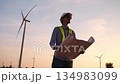 The engineer held the blueprints and looked around the field of wind turbines that were generating electricity. 134983099