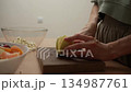 The image features a woman's hands skillfully cutting a crisp green apple on a wooden cutting board. As she prepares a wholesome and tasty fruit salad for a nutritious breakfast or a delightful snack 134987761