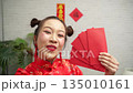 Happy young Asian woman in red cheongsam holding lucky red envelopes and taking a selfie with smartphone during Chinese New Year celebration Happy young Asian woman in red cheongsam holding lucky red envelopes and taking a selfie with smartphone during Chinese New Year celebration 135010161