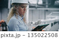 Female Industrial Engineer Wearing Hard Hat and Inspecting Production Data on Tablet 135022508