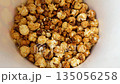 Eating caramel popcorn from cardboard bucket. The process of taking sweet popcorn from bucket. Hand picks up kernel of popcorn and takes it out of the bucket, close up 135056258