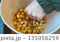 Close up footage of sweet popcorn being eaten from cardboard bucket. Hand reaches into popcorn bucket and pulls out kernel of caramel popcorn. Process of eating popcorn close up 135056259