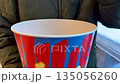 Hand takes kernel of popcorn from large cardboard bucket. The act of eating a pre movie snack. Concept of eating popcorn before the movie even starts. Eating popcorn outside the cinema 135056260