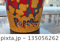 Bucket of popcorn with bright design on table. Packaging for your favorite movie theater snack. Watching a movie with popcorn. Huge portion of popcorn in cardboard bucket 135056262