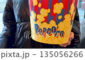 Bright, round bucket of popcorn featuring favorite movie snack. Girl holding popcorn as she goes to see a movie. Always grab some popcorn when you go to the cinema 135056266