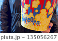 Woman hand adjusts large bucket of popcorn before heading to the cinema. Girl in warm jacket holds movie order. Winter trip to the cinema with bucket of popcorn 135056267