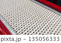Moving conveyor with white belt and red side. Plastic conveyor links for bending around curves in factory. Straight line with moving surface for transporting goods. Empty conveyor in motion 135056333