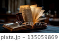 Wooden gavel and open law book on a courtroom desk with legal literature in the background 135059869