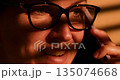 Close-up of Person with Glasses Talking on Phone in Warm Lighting 135074668