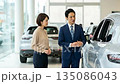 Asian Salesman in Suit Showing New Car Features to Female Customer in Showroom 135086043