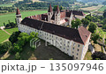 Aerial summer scenery of Sankt Paul im Lavanttal with monastery complex, rooftops, valley landscape, green hills, calm cinematic drone movement, warm atmospheric tones 135097946