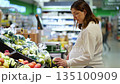 Brunette pregnant woman chooses green apples in supermarket 135100909