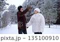 Mature couple walks in snowy forest and shares warm smiles 135100910