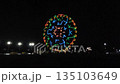 A beautiful huge Ferris wheel shines in the amusement park. Evening amusement park. Glowing attractions. 135103649