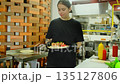 Female chef in black t-shirt puts sushi roll onto metal counter 135127806