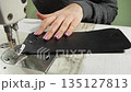 Needlewoman takes piece of leather out of machine stand 135127813