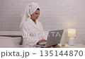 Bedroom office, Woman working, Digital nomad. Woman working on laptop while sitting in bedroom, dressed in bathrobe 135144870