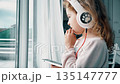 Child listening to music with headphones at home by window 135147777